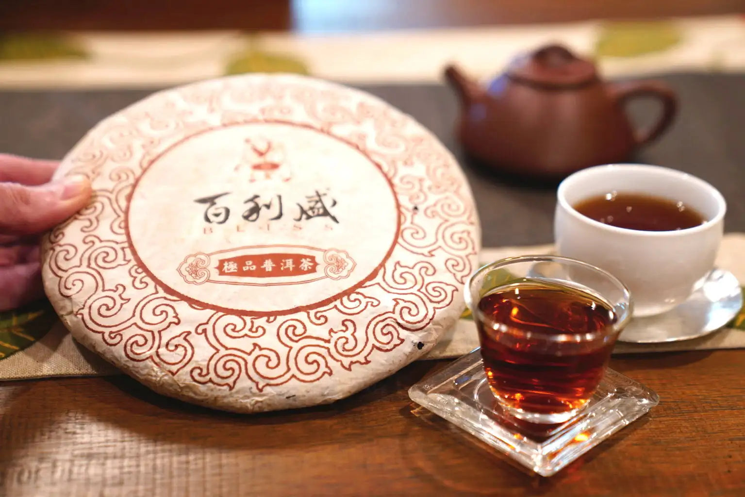 A round, compressed tea cake wrapped in ornate white and reddish-brown paper with chinese characters and decorative swirls.