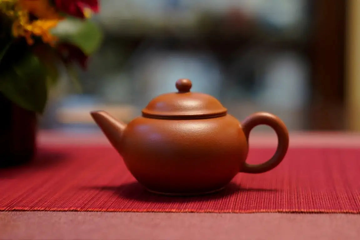 A smooth, terracotta-colored clay teapot with a rounded body and matching lid.