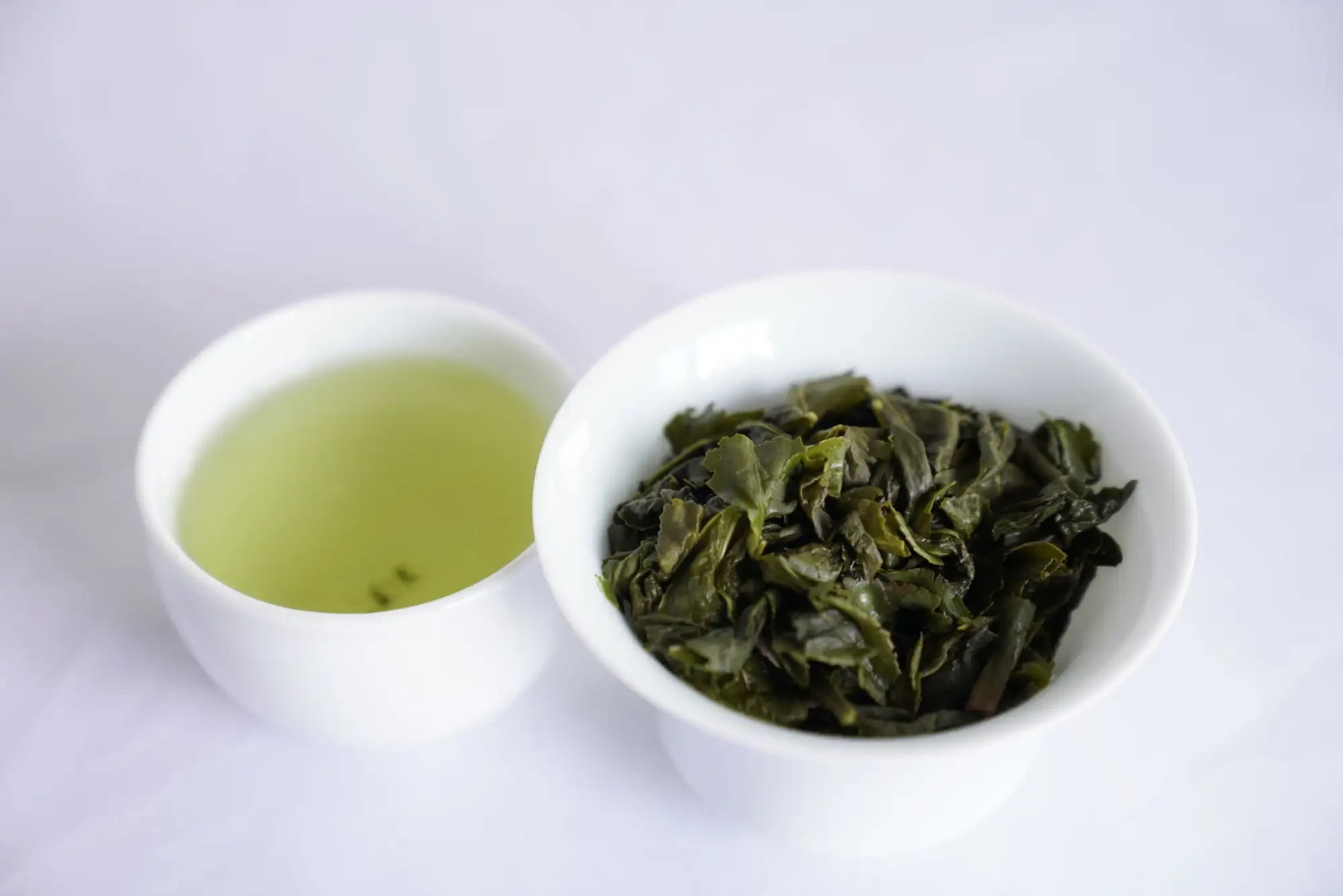 White ceramic bowl filled with dark green, curled tea leaves.