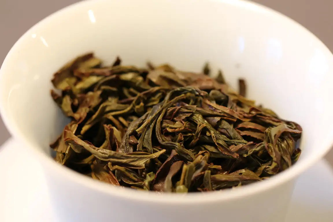 A white ceramic bowl filled with dried, dark green and brown tea leaves.